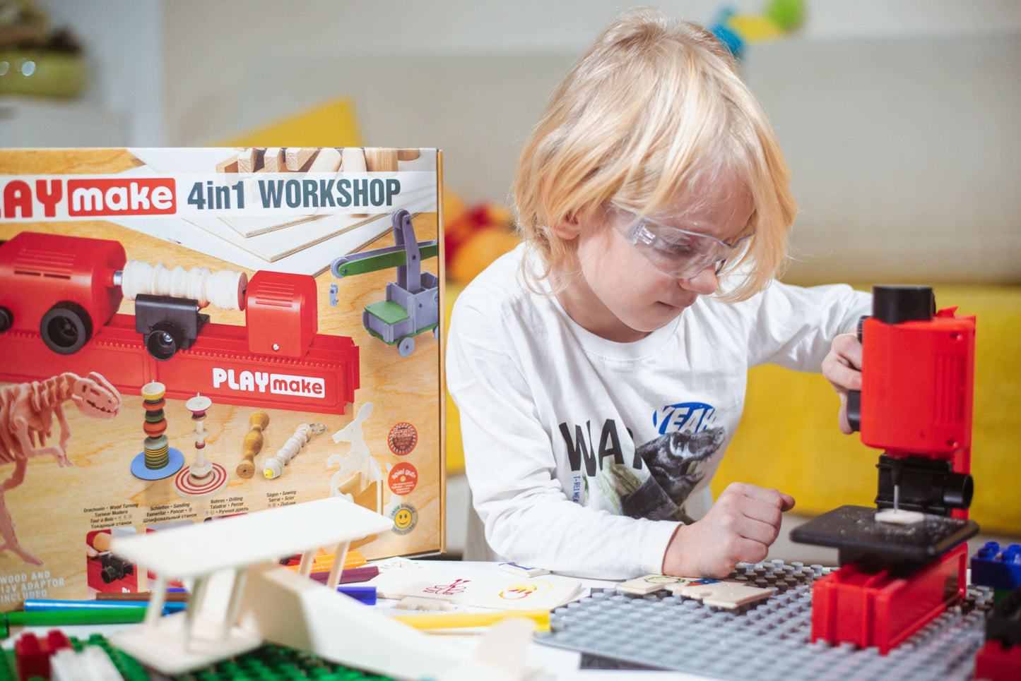 Kind bohrt mit der PLAYmake Stichsäge neben der Produktverpackung und Holzmodellen auf einem Tisch