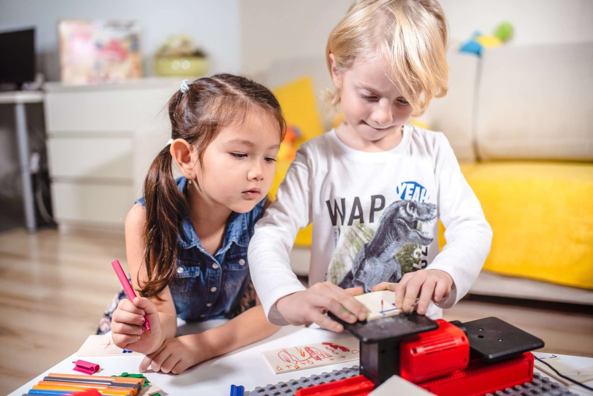 2 Kinder spielen mit der PLAYmake Stichsäge auf einem Tisch